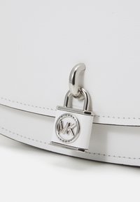 Borsa bianca con un lucchetto silver e un dettaglio circolare del logo. Materiale in pelle liscia con dettagli cuciti e una finitura lucida.