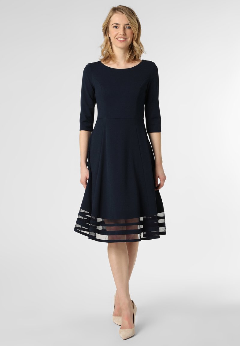 Marineblaues Kleid mit tailliertem Oberteil, 3/4-Ärmeln und einem ausgestellten Rock, der einen transparenten, geschichteten Saum mit horizontalen Streifen aufweist. Glatte Textur.