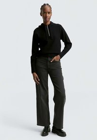 Juodas užsegamas gobtuvu su kapišonu, derinamas su tamsiai pilkais plačiomis kojomis džinsais. Abu drabužiai pagaminti iš minkštos, tekstūruotos medžiagos ir pasižymi minimalistiniu dizainu.