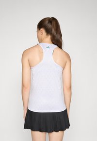 Bjela atletska majica s mrežastom teksturom i dizajnom s racerback, s malim tirkiznim logotipom. Uparen s crnom plisiranom suknjom.