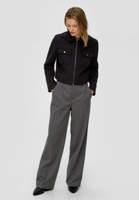 Czarna kurtka z zamkiem błyskawicznym z dwoma przednimi kieszeniami, zestawiona z szarymi spodniami typu wide-leg oraz czarnymi szpilkami. Gładka faktura materiału.