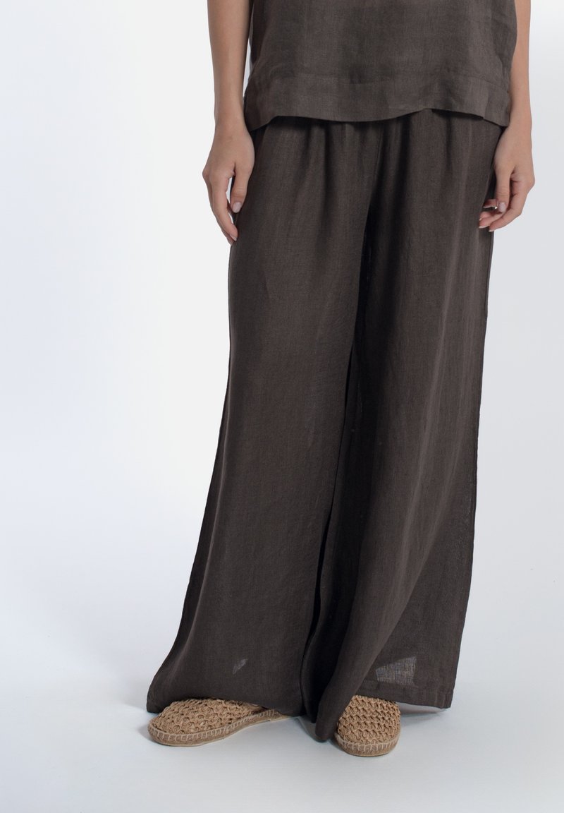 Pantaloni di lino marrone scuro, larghi e con una vestibilità relax, abbinati a scarpe slip-on in paglia beige.