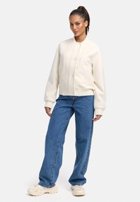 Witte bomberjack met ronde kraag, geribbelde manchetten en twee zijzakken, gecombineerd met losse blauwe jeans en crèmekleurige sneakers.