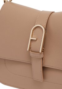 Borsa a mano in pelle beige con una superficie liscia, dotata di una fibbia in metallo dorato e una chiusura a pattina. Dettagli di cucitura evidenti lungo i bordi.