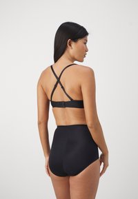 Zwarte bh met kruisbanden en een haaksluiting. Hoge taille zwarte slips. Glad textuur, minimalistisch ontwerp en geen zichtbare patronen.
