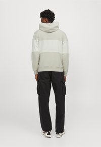 Sudadera gris claro con rayas blancas horizontales, con una gran capucha y puños acanalados, combinada con pantalones cargo negros.