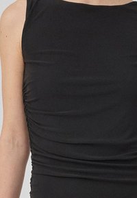 Svart ermeløs topp med samlet side-detaljering. Glatt, elastisk stoff med et tettsittende design, med rund hals.