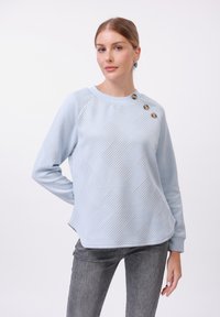 Felpa azzurra con motivo a zigzag testurizzato, scollatura rotonda, tre bottoni decorativi sulla spalla sinistra e polsini a costine.