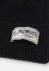 Juoda raštuota megzta kepurė su balta etiketė, kurioje užrašyta "Fiorucci Milano Since 1967" ir grafika. Tekstūruota medžiaga.