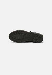 Semelle de chaussure noire avec motif de bande de roulement, étiquetée "TOMAR", affichant la taille 47, sur un fond gris clair uni.