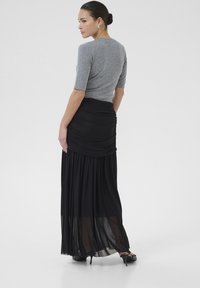 Grijze fitted top met korte mouwen, gecombineerd met een zwarte, vloeiende maxi-jurk met geplooide details en een doorschijnende onderlaag.