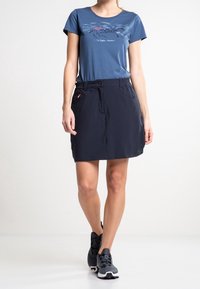 Marinblå kjol med elastisk midja och framfickor, tillsammans med en blå t-shirt med grafiskt tryck som har bergmotiv i nyanser av rosa och blått.