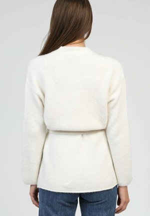 Pull en laine de couleur crème à manches longues, avec une coupe ample et une ceinture à nouer à la taille, présentant une texture douce et un ourlet arrondi.