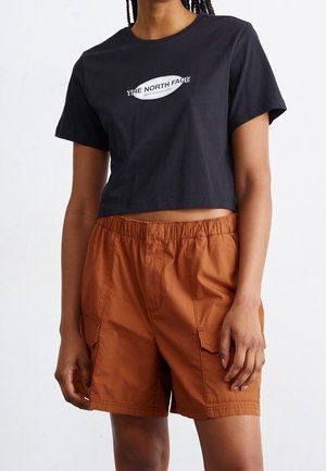 Osoba nosząca czarny krótki t-shirt z logo "The North Face" oraz rdzawe szorty typu cargo z elastycznym pasem i przednimi kieszeniami.
