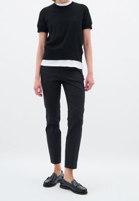 Black short-sleeve sweater layered over a white shirt, paired with black slim-fit pants and black loafers; smooth textures and simple design.