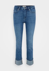 Blå denimjeans med frontlommer, knappelukking og oppbrettede cuffs mot en enkel lys bakgrunn.
