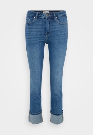 Jeans in denim blu con tasche frontali, chiusura a bottone e orli arrotolati su uno sfondo chiaro e semplice.