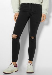Jeans negros ajustados con desgastes en las rodillas, diseño de tiro alto y corte slim. Combinados con zapatillas blancas con acentos en color burdeos.
