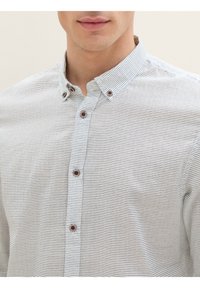 Camicia bianca con righe nere sottili, dotata di colletto aperto e bottoni marroni. Tessuto dalla consistenza liscia, vestibilità su misura.