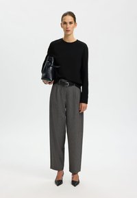 Black long-sleeve shirt, gray high-waisted trousers with a check pattern, and black pointed-toe heels. Holding a black structured handbag.