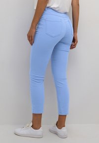Vaqueros ajustados de color azul claro con una cintura de altura media, bolsillos traseros y una textura suave, combinados con zapatillas blancas.
