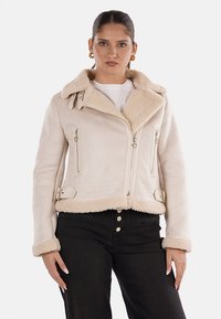 Giacca finta shearling beige, design cropped, con un ampio colletto e tasche con zip. Presenta dettagli con fibbie e una morbida fodera testurizzata.