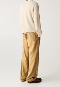 Maglione beige in maglia con vestibilità rilassata, abbinato a pantaloni cargo larghi di colore marrone chiaro con molteplici tasche e una texture liscia.