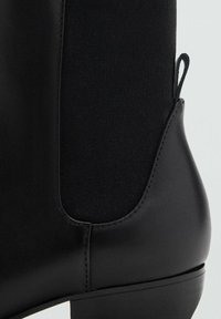 Stivale Chelsea in pelle nera con pannello elastico ai lati e linguetta di rilascio su uno sfondo chiaro e semplice.