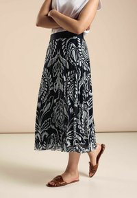 Czarna i biała plisowana spódnica w kwiatowy wzór, z elastycznym pasem, noszona z brązowymi płaskimi sandałami. Gładka, lekka tkanina, długość do kostek.
