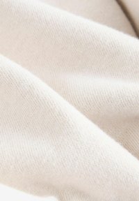 Světlý béžový pletený materiál s jemnou texturou, který se vyznačuje jemným žebrovaným vzorem. Povrch se zdá být hladký a mírně pružný.