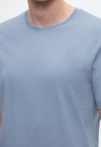 Šviesiai mėlynas trumpomis rankovėmis marškinėliai iš minkštos medvilnės. Turi apvalų kaklo iškirpimą ir subtilų siuvinėtą logotipą ant krūtinės. Lygus paviršius.