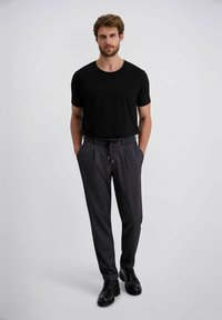 Zwart T-shirt met korte mouwen, gecombineerd met gestreepte donkere broek met een elastische tailleband en zijzakken, aangevuld met zwarte schoenen.
