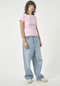 Helles rosa, kurzärmliges, tailliertes T-Shirt, kombiniert mit lockeren, hellblauen Jeans mit hoher Taille und sichtbaren Nähten. Weiße Sneakers.