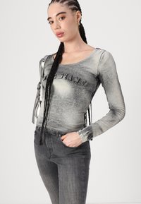 Haut gris à manches longues, ajusté, avec une finition texturée et "JEANS" brodé à l'avant. Associé à un jean gris foncé au design minimaliste.