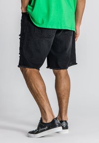 Pantalones cortos de mezclilla negra con dobladillo deshilachado, con bolsillos laterales; combinados con una camiseta verde brillante y zapatillas negras.