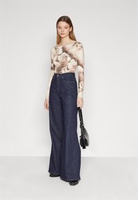 Long-sleeve top with a light brown abstract print, paired with high-waisted dark blue wide-leg jeans and a black handbag. Smooth texture.