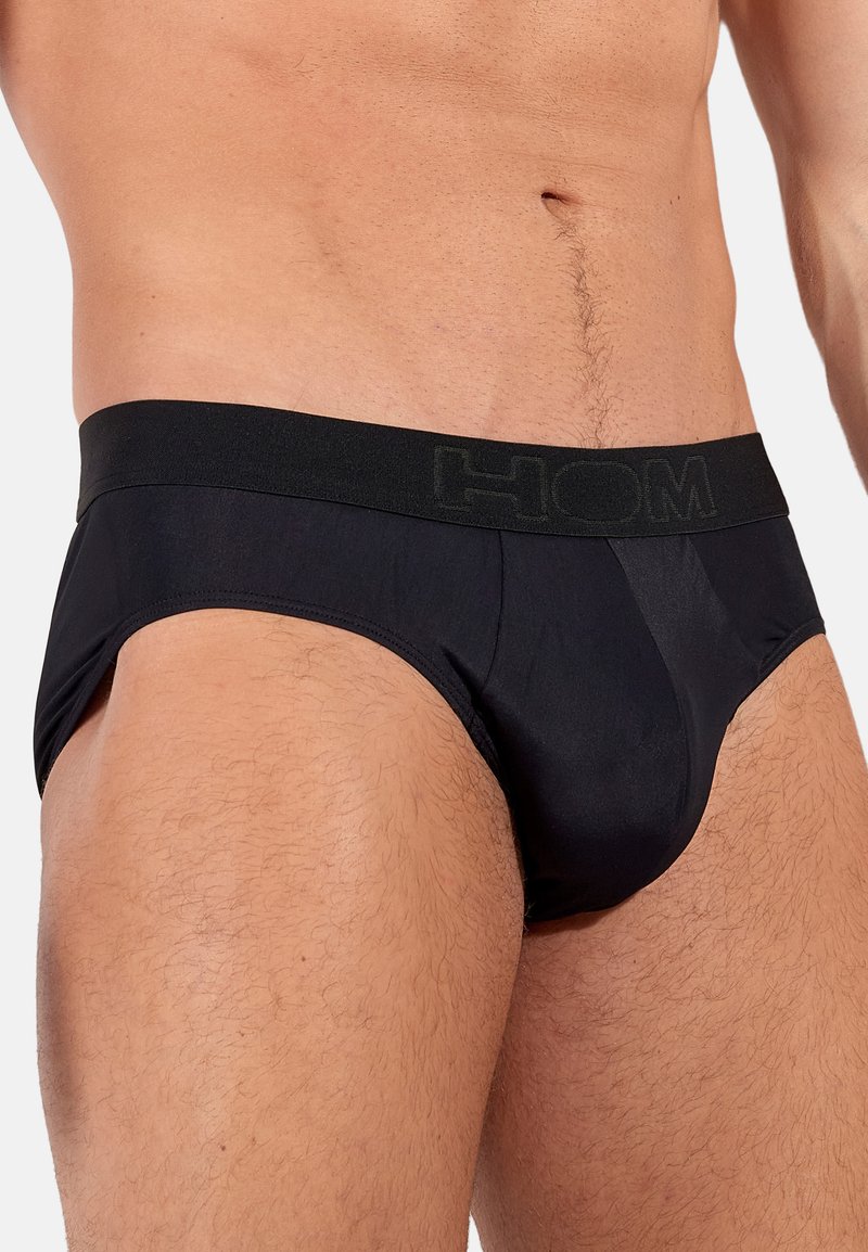 Zwarte herenonderbroeken van glad materiaal, met een brede zwarte tailleband waarin het merk 'HOM' is geperst. Eenvoudig en lichaamsvolgend ontwerp.