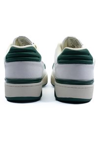 Bijele i zelene tenisice s zamšastim i teksturiranim detaljima, podstavljenim okvirom pete i kontrastnom potplatom. Imaju zaobljen vrh i debeli potplat.