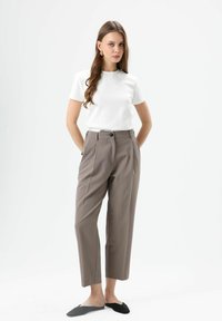 Witte top met korte mouwen gecombineerd met lichtbruine, hoog getailleerde broek. De broek heeft een knoopsluiting en is licht gecropped. Zwarte instapschoenen.