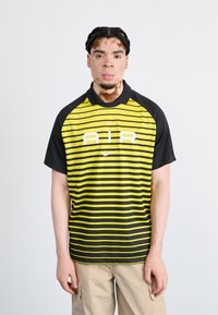 Nike krekls ar horizontālām melnām un dzeltenām svītrām, melnu apkakli un baltu "AIR" logo priekšpusē. Īsas piedurknes, sportisks griezums.