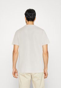 T-shirt in cotone beige con collo a giro e maniche corte, vista dal retro. Tessuto liscio, vestibilità comoda e senza motivi visibili.