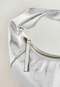 Strieborná metalická kabelka vyrobená z textúrovaného materiálu, s zlatým zipsom a skrútenou rukoväťou. Kompaktne tvarovaná s minimalistickým dizajnom.