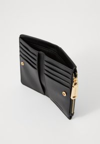 Portefeuille en cuir noir avec plusieurs emplacements pour cartes, accents en hardware doré, fermeture éclair, texture lisse et détail de logo à l'extérieur.