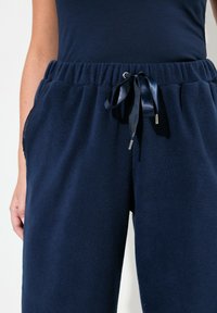 Laatikko fleece-housut, joissa on joustava vyötärö, kiristettävä naru ja sivutaskut. Pehmeä rakenne ja rento istuvuus mukavuuden takaamiseksi.