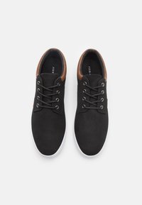 Baskets en toile noires avec des accents en cuir marron, bout rond et semelle en caoutchouc blanc. Comprend six œillets et des lacets noirs.