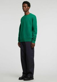 Zielony sweter z dzianiny z długimi rękawami i okrągłym dekoltem, zestawiony z ciemnoniebieskimi szerokimi spodniami i czarnymi butami. Prosty design i faktura.