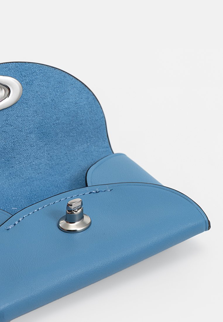 Blauwe leren handtas met een zachte textuur, rond flapontwerp, sluiting met zilveren hardware en contrasterende stiksels.