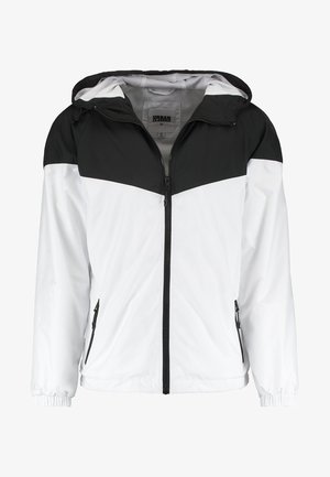 Veste pour homme avec une partie supérieure noire et une partie inférieure blanche, fabriquée dans un matériau lisse et léger, dotée de poches zippées et d'une capuche.