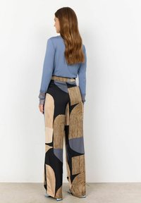 Ursnygga, högmidjade svarta byxor med geometriska mönster i beige och marinblått; kombinerade med en blå långärmad topp med spetsdetaljer.