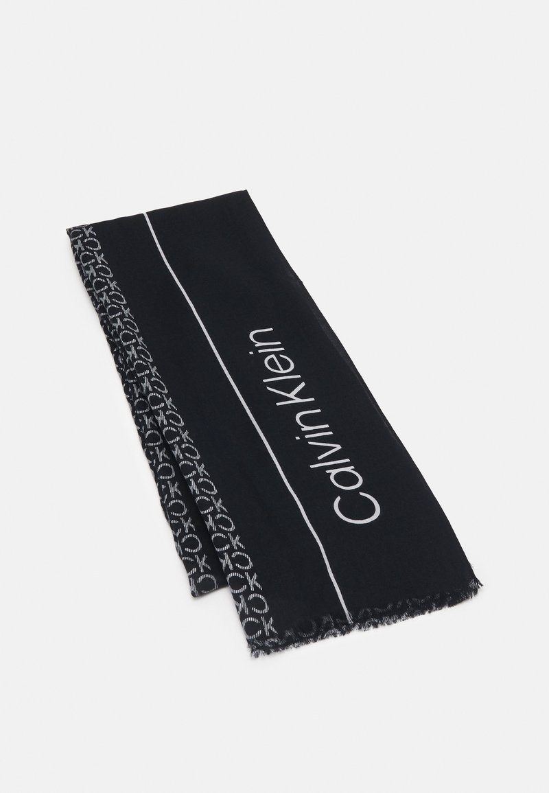 Écharpe en tissu noir pliée, arborant le texte blanc "Calvin Klein" et un bord orné de petits logos blancs.